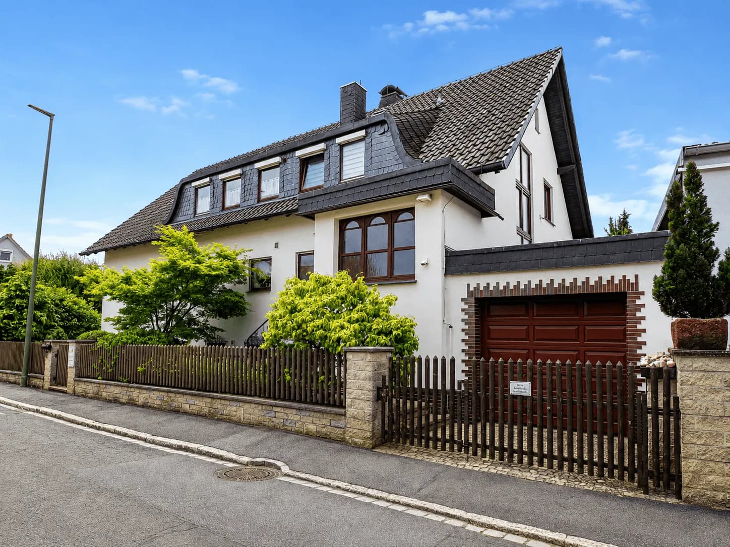 Gepflegtes Einfamilienhaus mit ausgebautem Mansarddach, angebauter Garage, Holzzaun und grünem Vorgarten: Straßenansicht in Burgkunstadt.