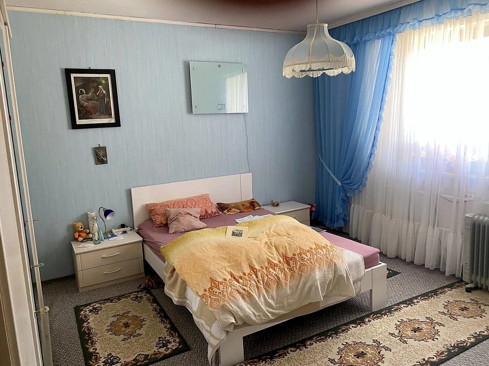 Helles Schlafzimmer mit Doppelbett, zwei Nachttischen, modernem Wandheizkörper und großem Fensterbereich mit wohnlicher Fensterdekoration.