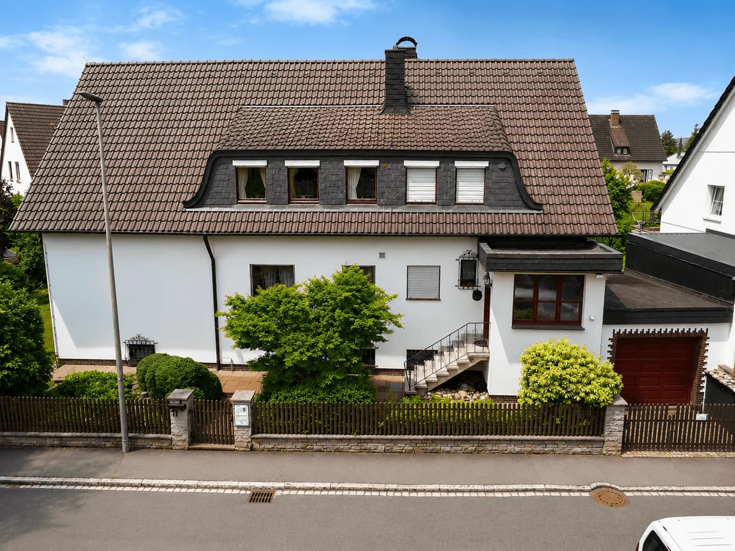 Frontale Drohnenaufnahme eines gepflegten Einfamilienhauses mit Mansard-Dachgaube, Tondachziegeln, Außentreppe, Garage und eingezäuntem Vorgarten in Burgkunstadt.