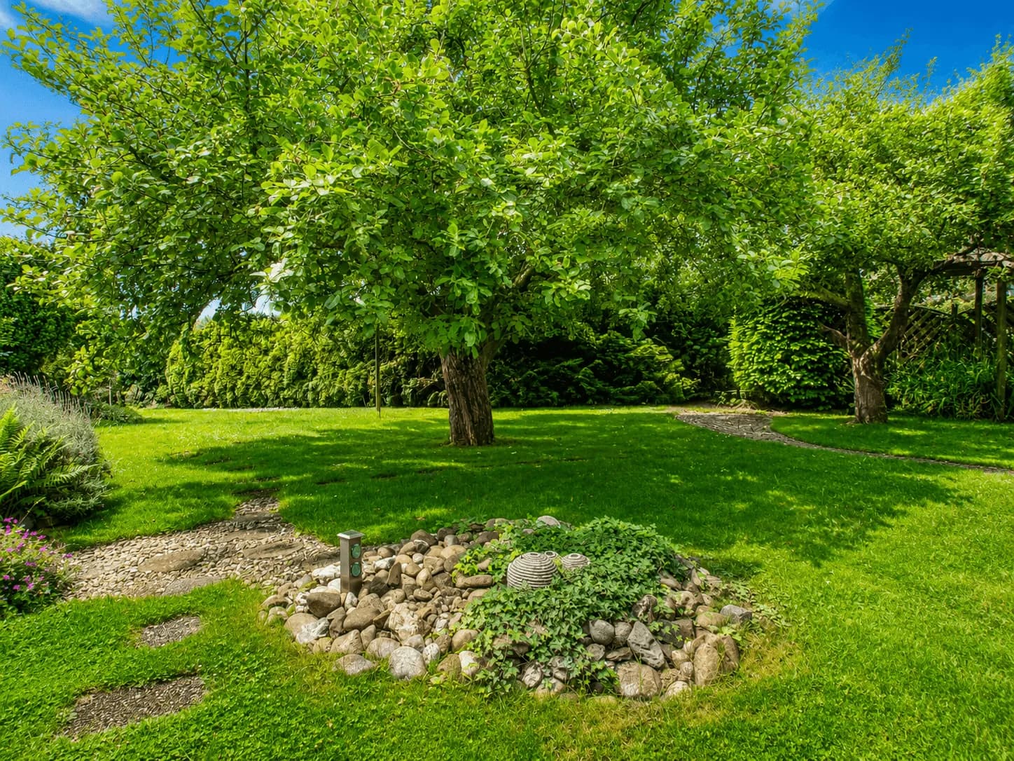 Gepflegter, weitläufiger Garten mit sattgrüner Rasenfläche, schattenspendenden Obstbäumen, Kieswegen und dekorativem Steingarten-Element in Burgkunstadt.
