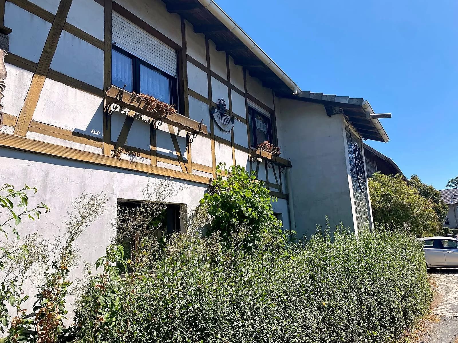 Charaktervolle Außenansicht der Immobilie mit sichtbaren Fachwerkelementen, Zierschmiedekunst, Blumenkästen und gepflegter grüner Hecke.