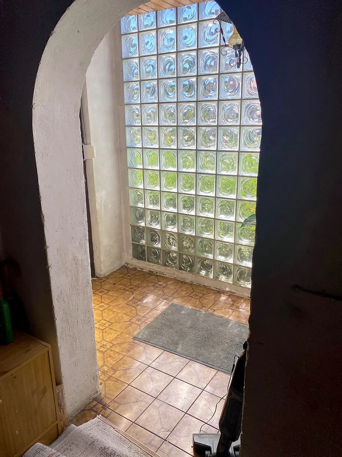 Eingangsbereich mit rundbogigem Durchgang, gefliestem Boden und lichtdurchfluteter Glasbausteinwand für ein helles Entree.