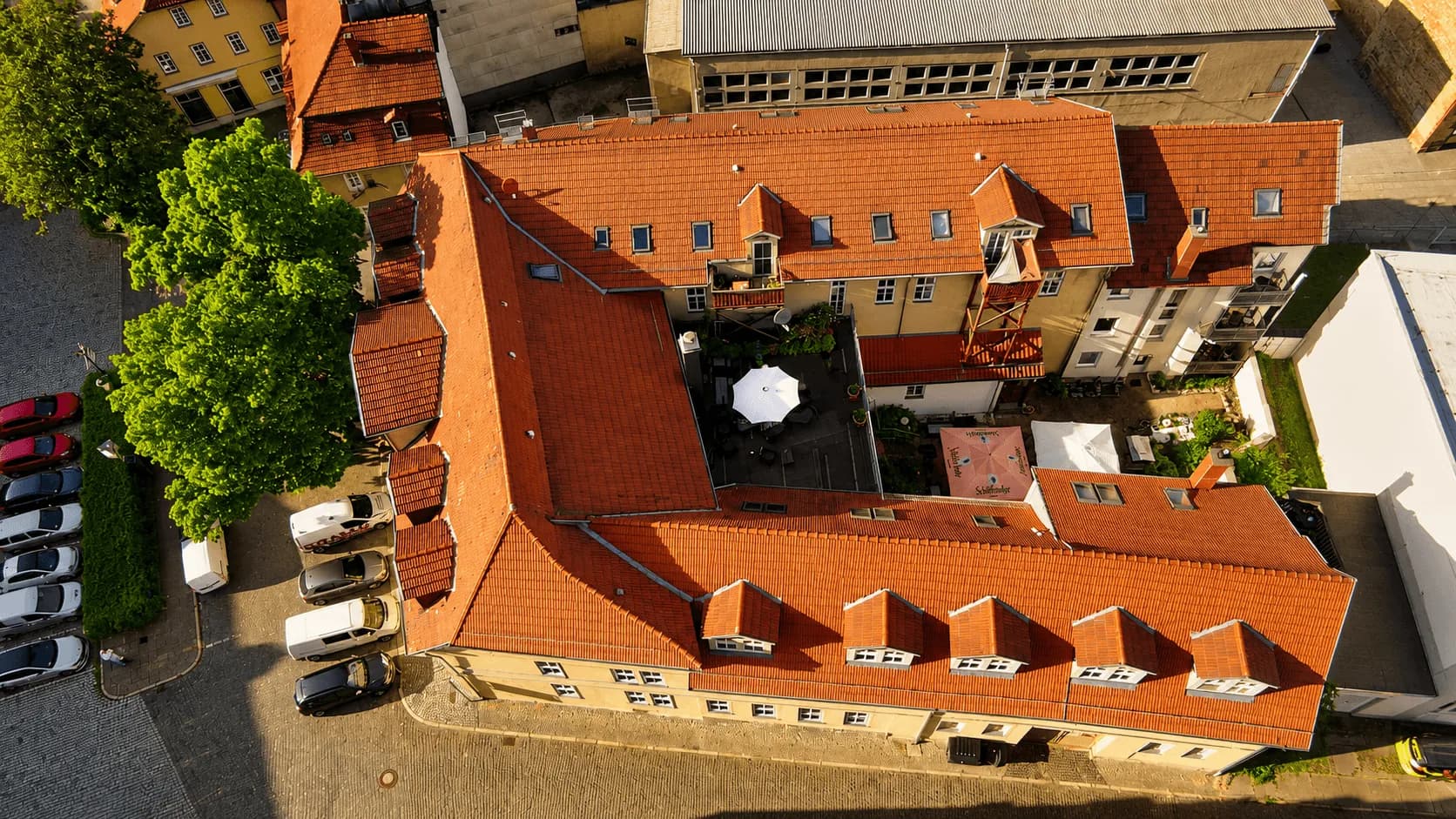 Schrägluftaufnahme des historischen Ensembles im Stadtkern mit langgestrecktem Haupttrakt, traditioneller roter Ziegeleindeckung, verwinkeltem Innenhof und Blick auf den Marktplatz.