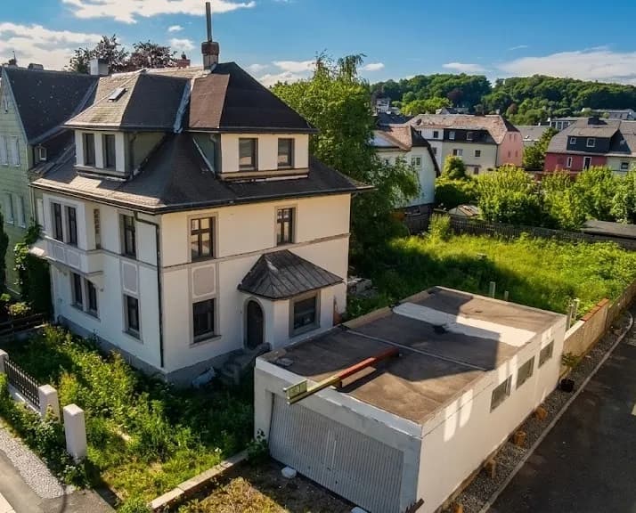 Vogelperspektive auf das Mehrfamilienhaus mit separatem Garagengebäude, Gartenbereich und grüner Nachbarschaft.