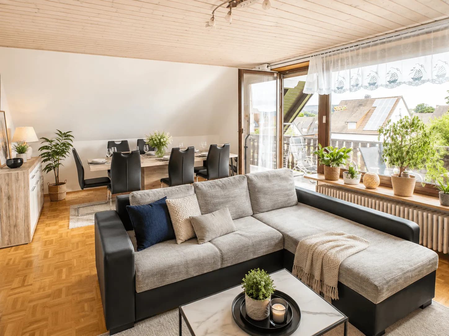 Lichtdurchfluteter Wohn- und Essbereich im Obergeschoss mit heller Holzdecke, grauer Eckcouch, Esstischgruppe, Parkettboden und Zugang zum Balkon in Burgkunstadt.