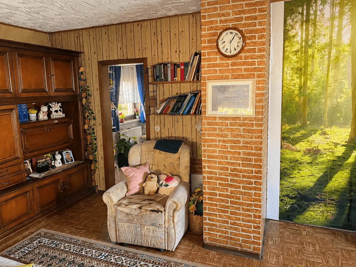 Gemütliche Leseecke im Wohnzimmer mit Polstersessel, Bücherregalen, Holz-Wandverkleidung und rustikaler Klinkersäule.