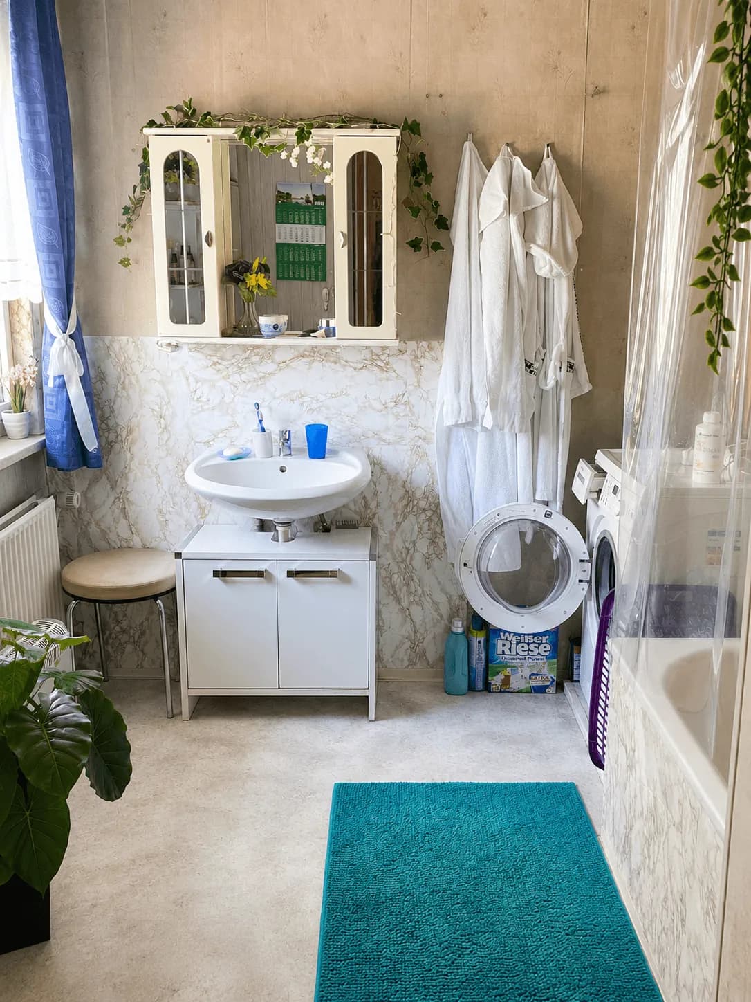 Helles Badezimmer mit Badewanne, Waschtisch mit Unterschrank, Spiegelschrank, Waschmaschine und großem Tageslichtfenster.
