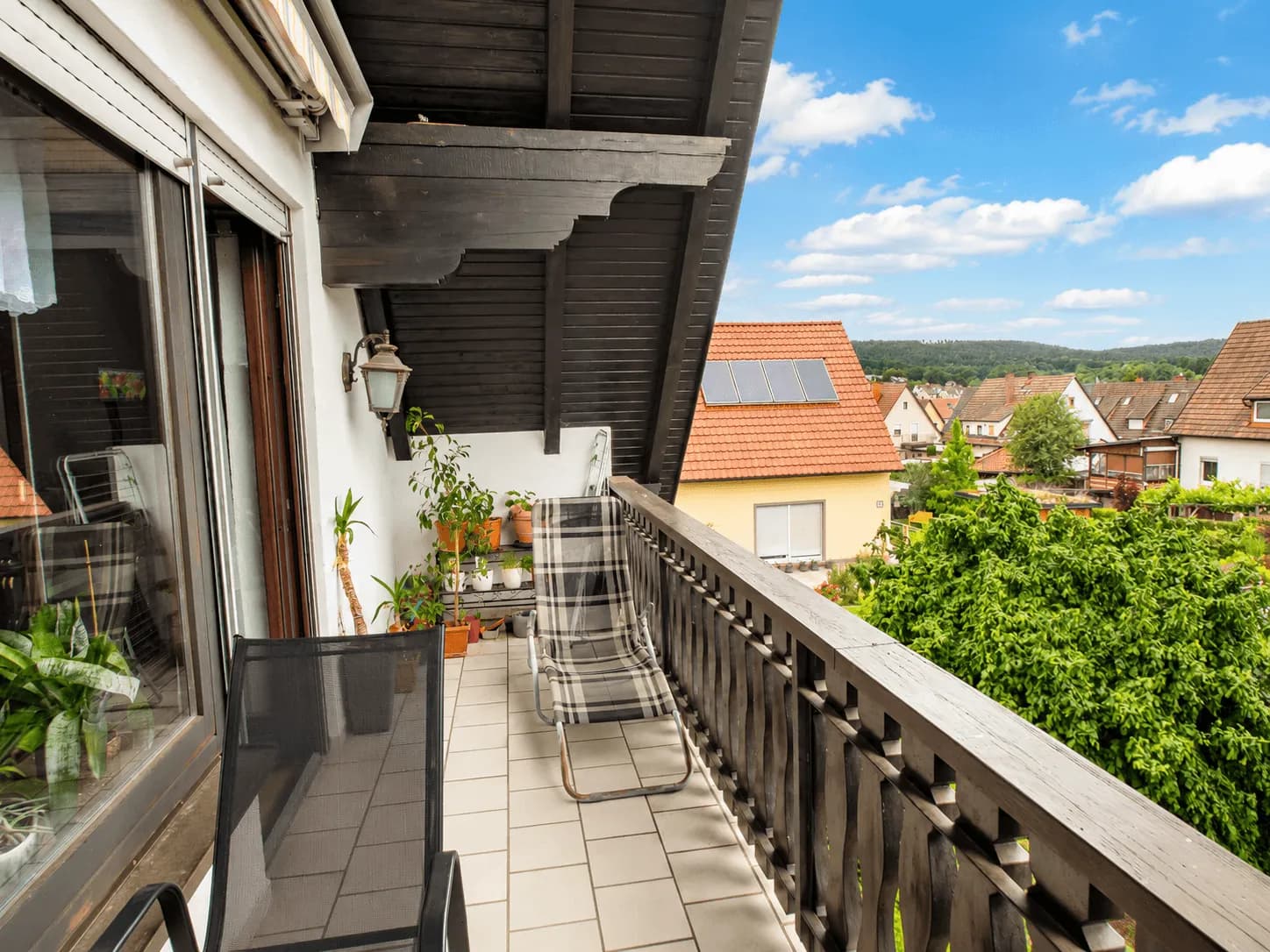 Gemütlicher Balkon im Obergeschoss mit traditionellem Holzgeländer, Sonnenliege, gefliestem Boden und Weitblick über die Dächer von Burgkunstadt.