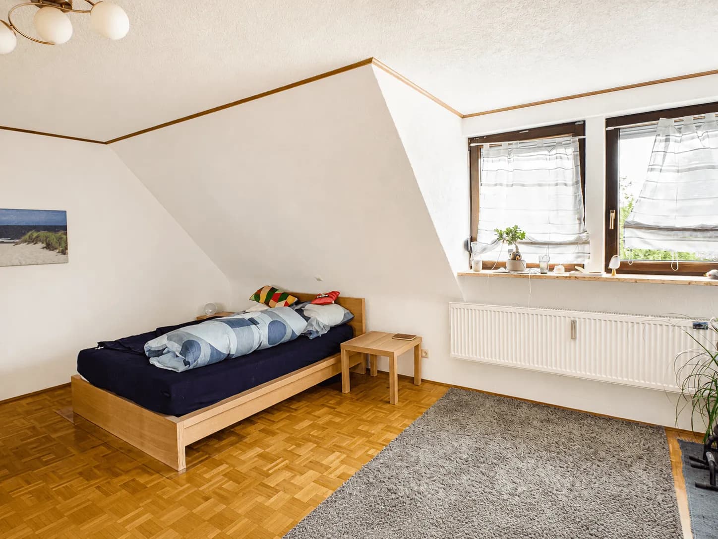 Helles und geräumiges Schlafzimmer im Dachgeschoss mit Dachschräge, Holzbett, Echtholzparkett und großen Fenstern in Burgkunstadt.
