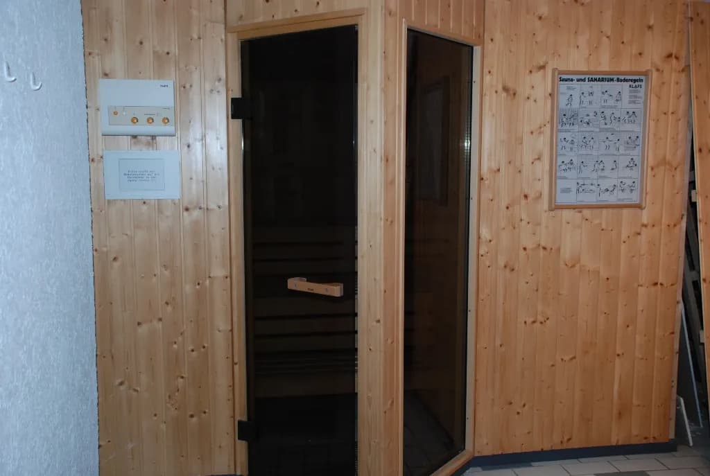 Eingebaute finnische Holzsauna mit hell strukturierter Holzvertäfelung, Glastür, elektronischem Steuergerät und Saunaregel-Übersichtstafel.