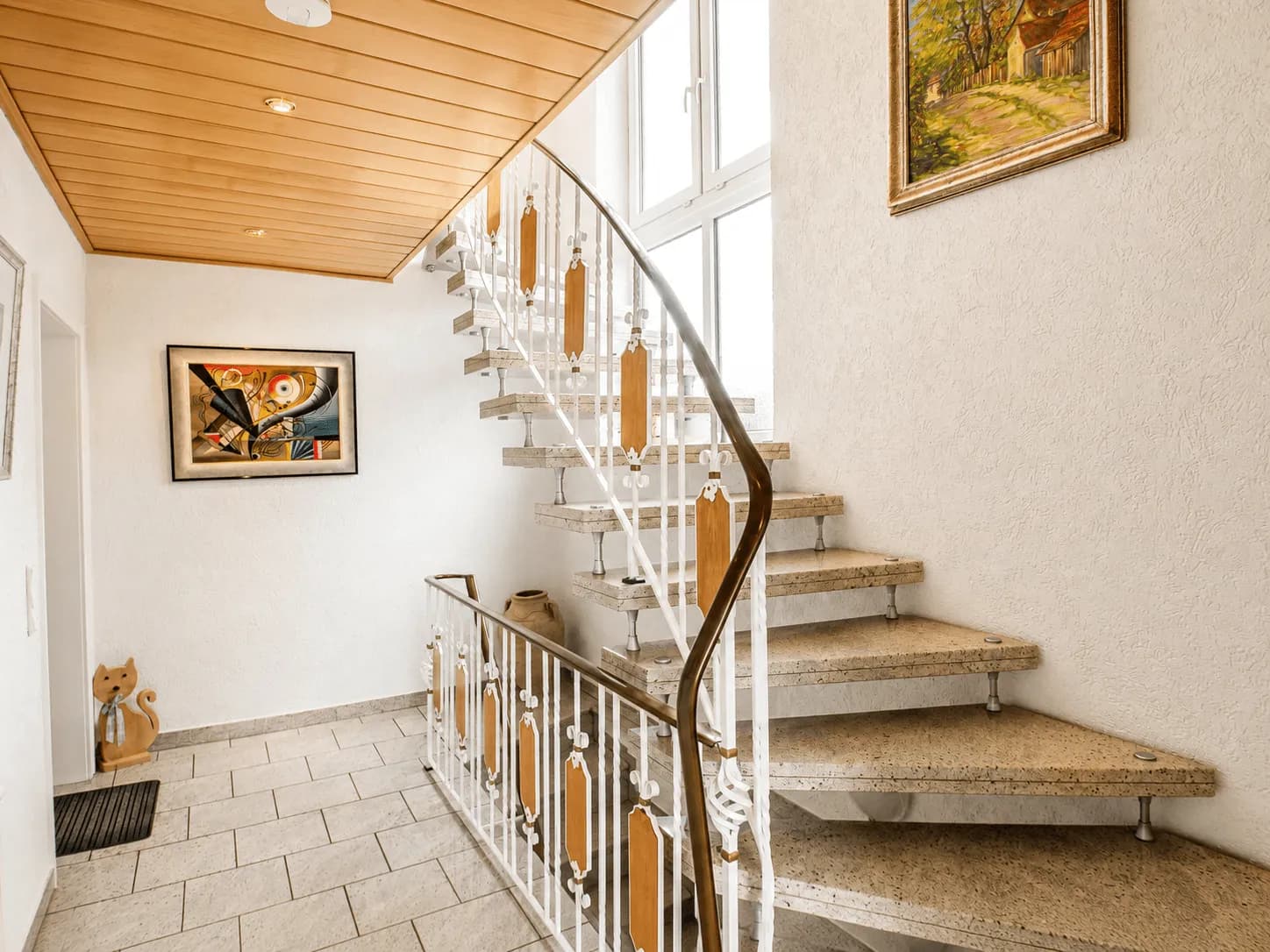 Heller Eingangsbereich und Flur mit offener Steintreppe, kunstvollem Geländer, gefliestem Boden und holzverkleideter Decke mit Einbaustrahlern in Burgkunstadt.