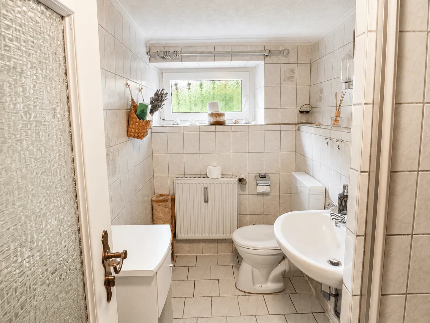 Hell gefliestes Gäste-WC im Untergeschoss mit Waschbecken, Toilette, Heizkörper und Tageslichtfenster in Burgkunstadt.