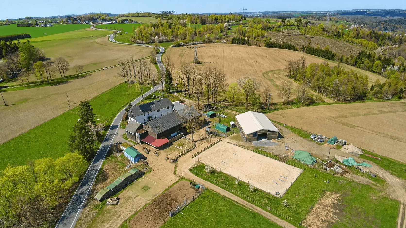 Weitläufige Panorama-Luftaufnahme des alleinstehenden Reiterhof-Anwesens inmitten von Feldern und Wiesen: Wohnhaus, Stallungen, Reithalle, Sandreitplatz und private Zufahrtsstraße.