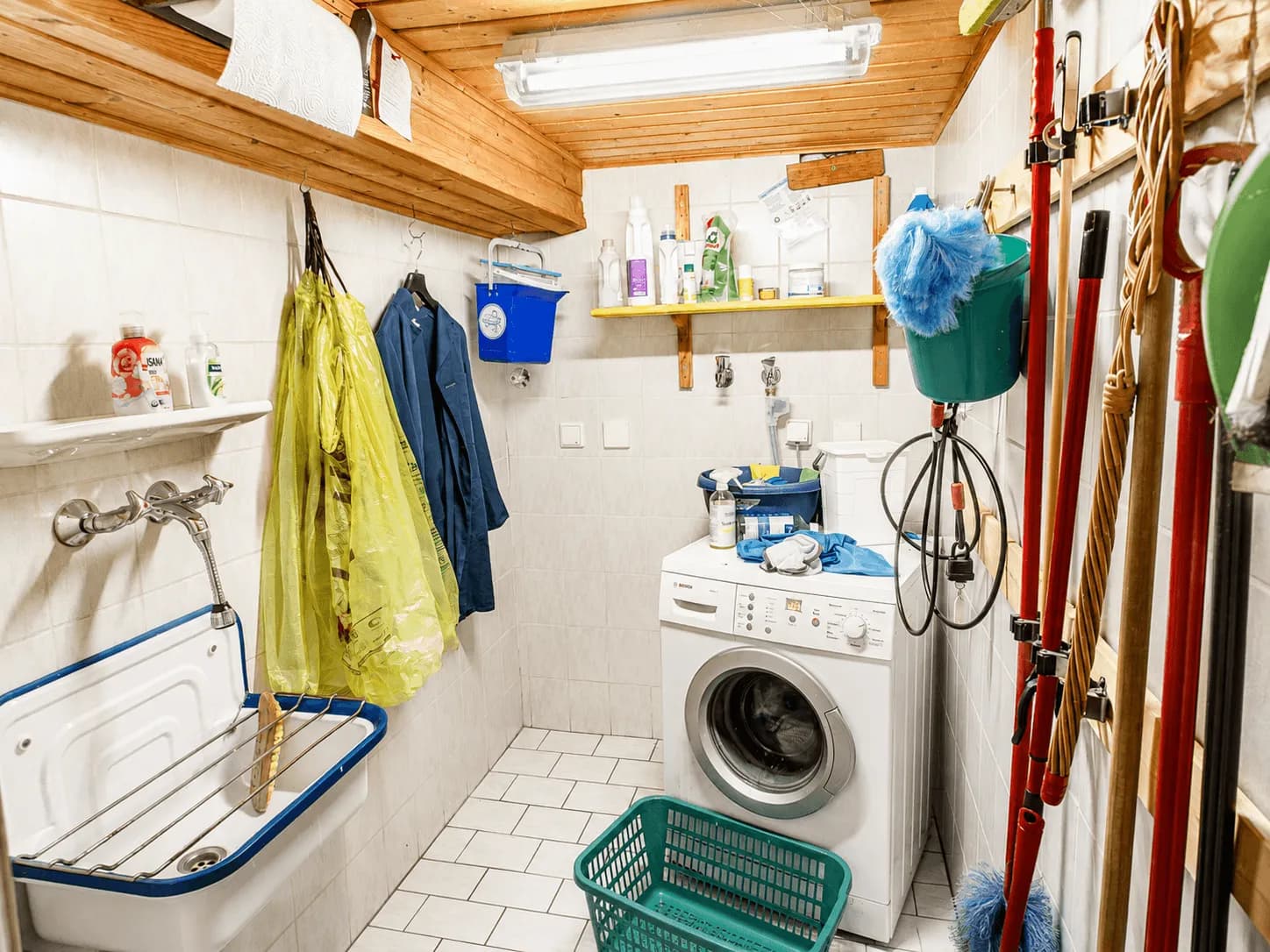Praktische Waschküche und Hauswirtschaftsraum im Untergeschoss mit Waschmaschine, Ausgussbecken, Ablagemöglichkeiten für Haushaltsutensilien und Holzdecke in Burgkunstadt.