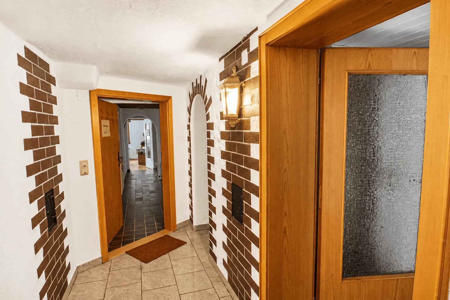 Flurbereich im Untergeschoss mit rustikalen Klinker- und Bogenelementen, dekorativer Wandlaterne, Holztüren und hellem Fliesenboden in Burgkunstadt.
