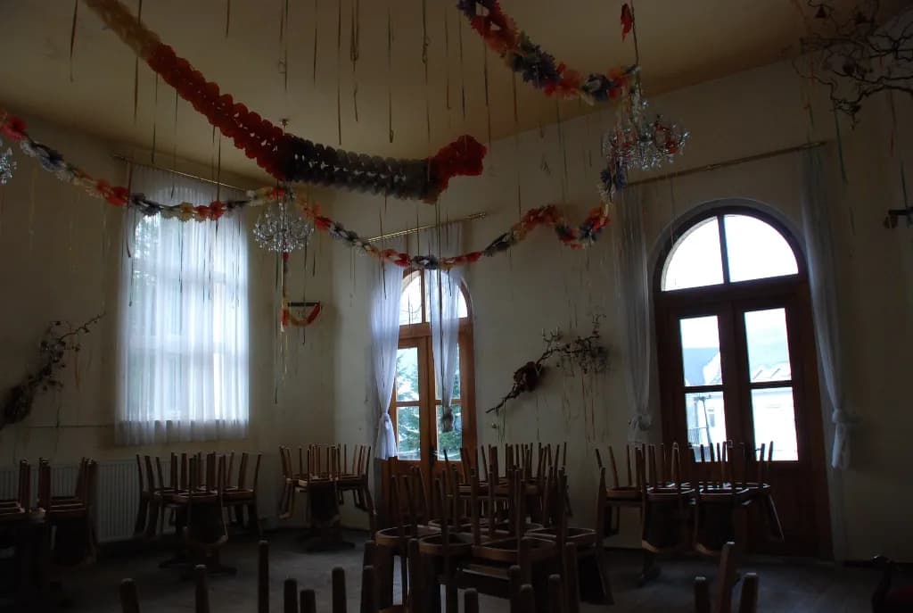 Historischer Festsaal mit hohen Rundbogenfenstern und Balkontüren, Kristallleuchtern, festlicher Dekoration und hochgestellten Holzstühlen.