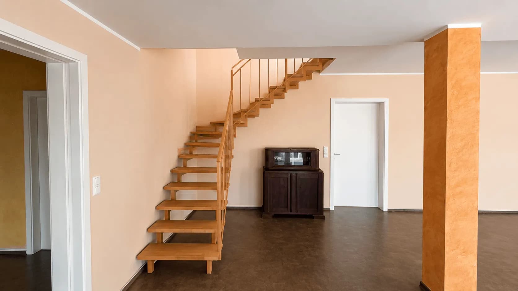 Geschwungene, offene Holztreppe mit Metallgeländer ins Obergeschoss als eleganter Blickfang im weitläufigen Wohn- und Dielenbereich.