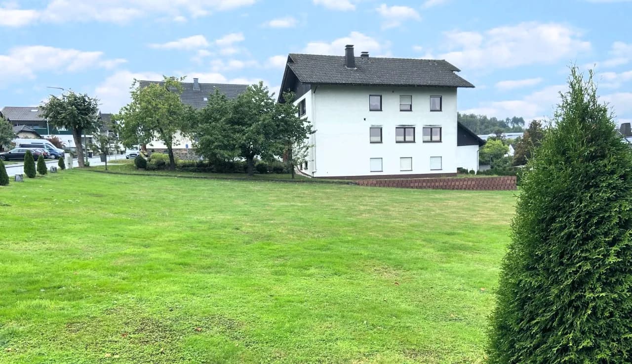 Gartenansicht des Wohnhauses mit weitläufigem Wiesengrundstück, gepflegtem Rasen, altem Obstbaumbestand und Ziertuja im Vordergrund.