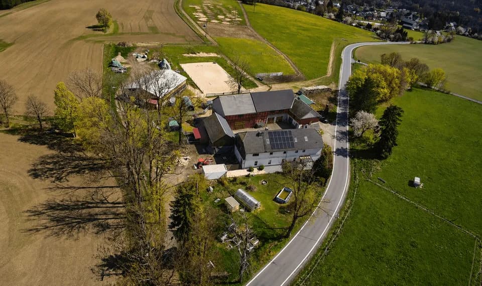 Vogelperspektive auf das weitläufige Reiterhof- und Resthof-Anwesen: Wohnhaus mit Photovoltaikanlage, Reitplatz, Stallungen und Nebengebäude, umgeben von Wiesen und Feldern an einer ruhigen Landstraße.