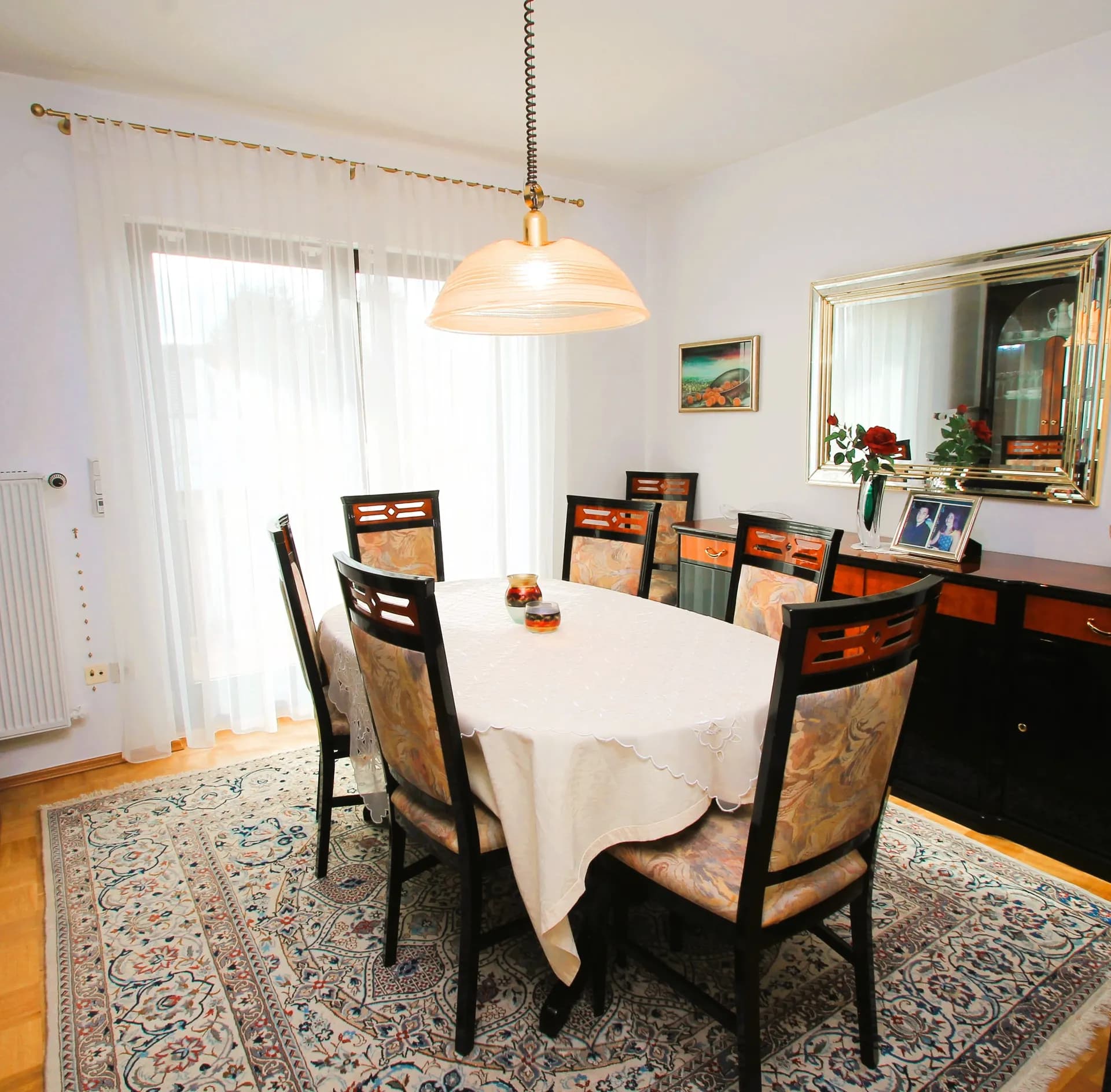 Stilvoller Essbereich des Wohnhauses mit ovalem Esstisch für sechs Personen, gepolsterten Holzstühlen, eleganter Anrichte mit großem Wandspiegel, Pendelleuchte und Orientteppich.  9.jpg