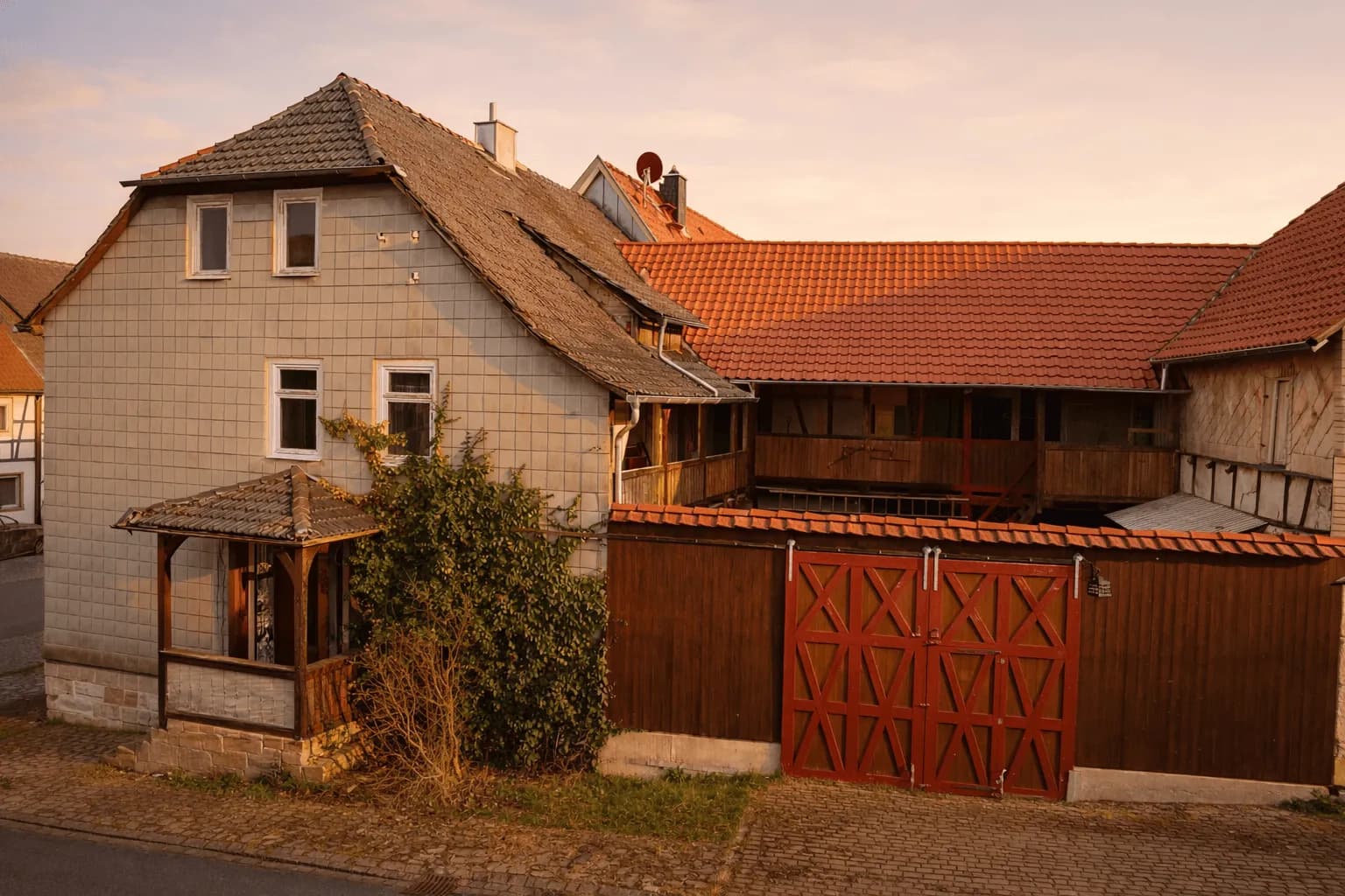 Hofansicht des Anwesens mit schieferverkleidetem Wohnhausteil, überdachtem Eingangspodest, hölzernen Laubengängen und massivem Hoftor.