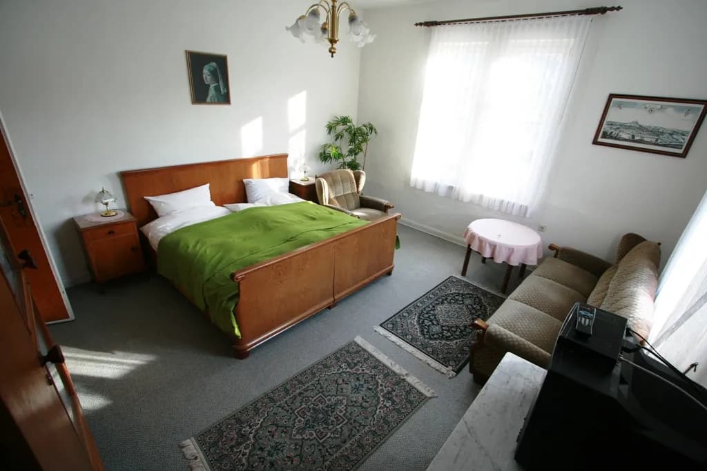 Gemütliches Gäste- oder Hotelzimmer im klassischen Stil mit Holzdoppelbett, Nachttischen, Polstersofa, Sessel, rundem Beistelltisch und Orientteppichen.