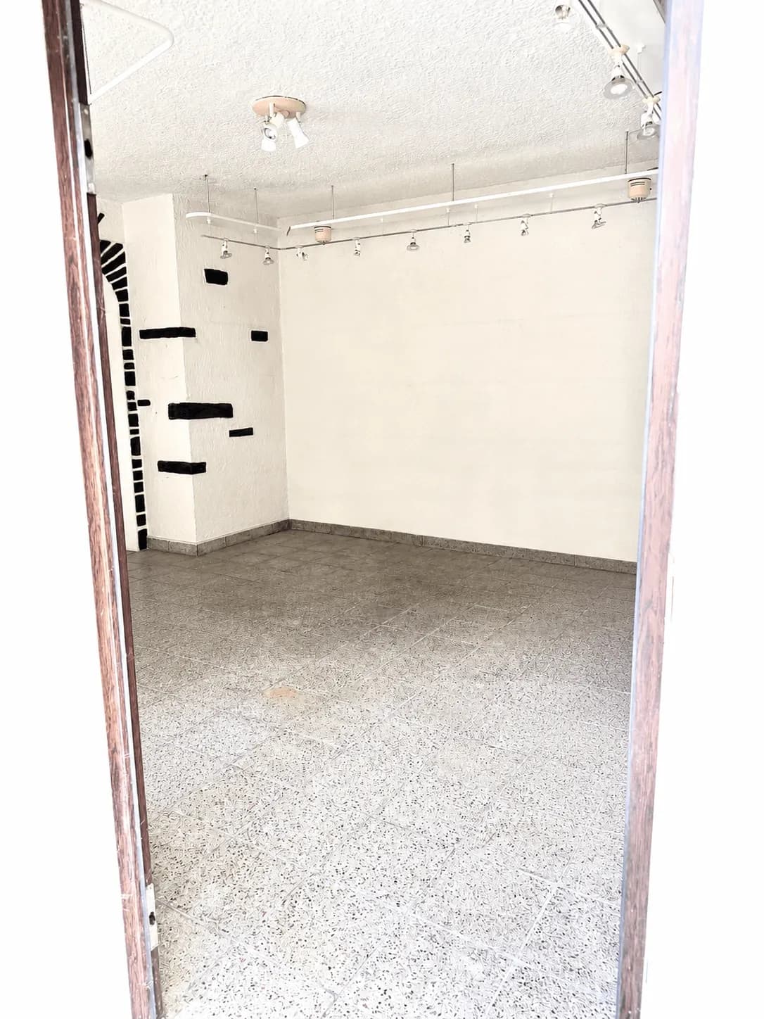 Heller, geräumiger Raum mit robustem Terrazzo-/Fliesenboden, weißen Wänden, professioneller Deckenspot-Beleuchtung und dezenten Wandakzenten.