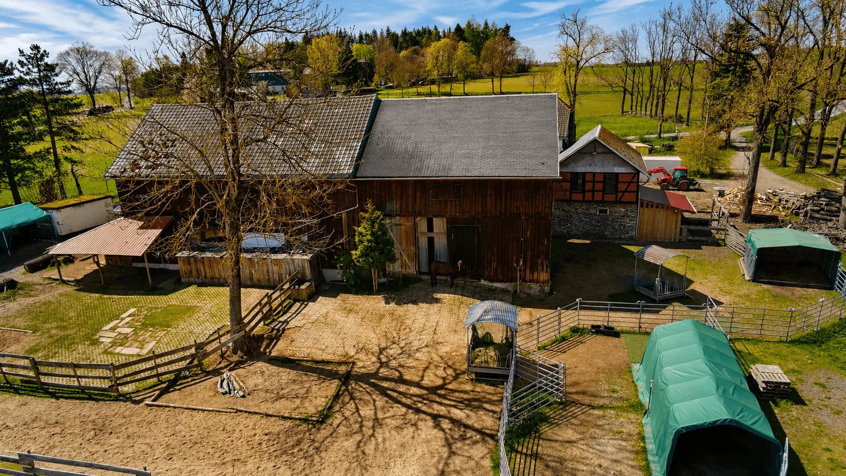 Luftaufnahme des Wirtschaftshofs der Reitanlage: massive Holzscheune mit angrenzendem Fachwerkgebäude, Paddocks, Weidezelten und Futterraufen.
