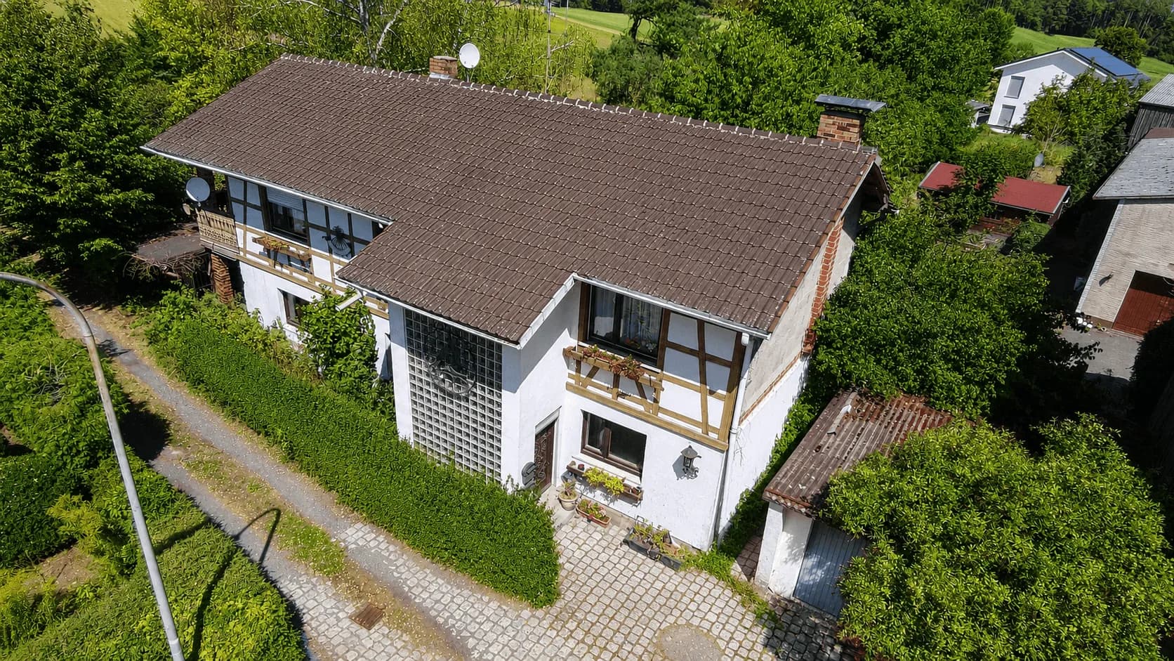 Drohnenperspektive des Wohnhauses mit Fachwerkelementen, eingewachsenem Grundstück, separater Garage und gepflasterter Hofeinfahrt in idyllischer Lage