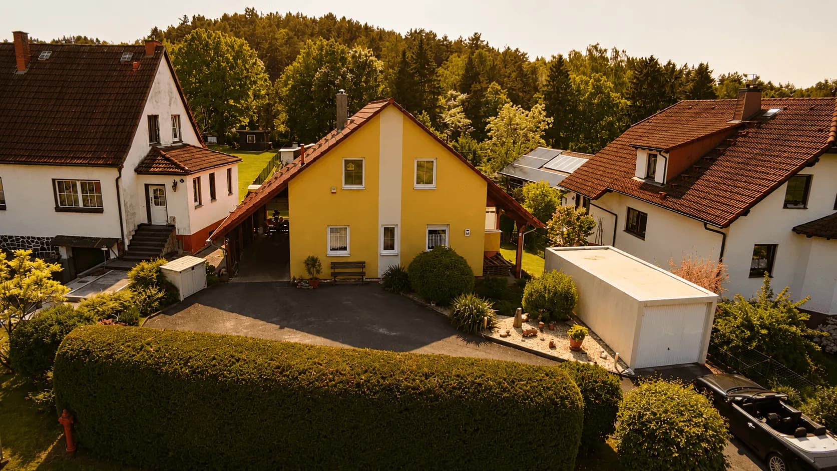 Luftaufnahme des Einfamilienhauses mit großem Gartengrundstück, eingezäunter Rasenfläche und Blick ins Grüne.