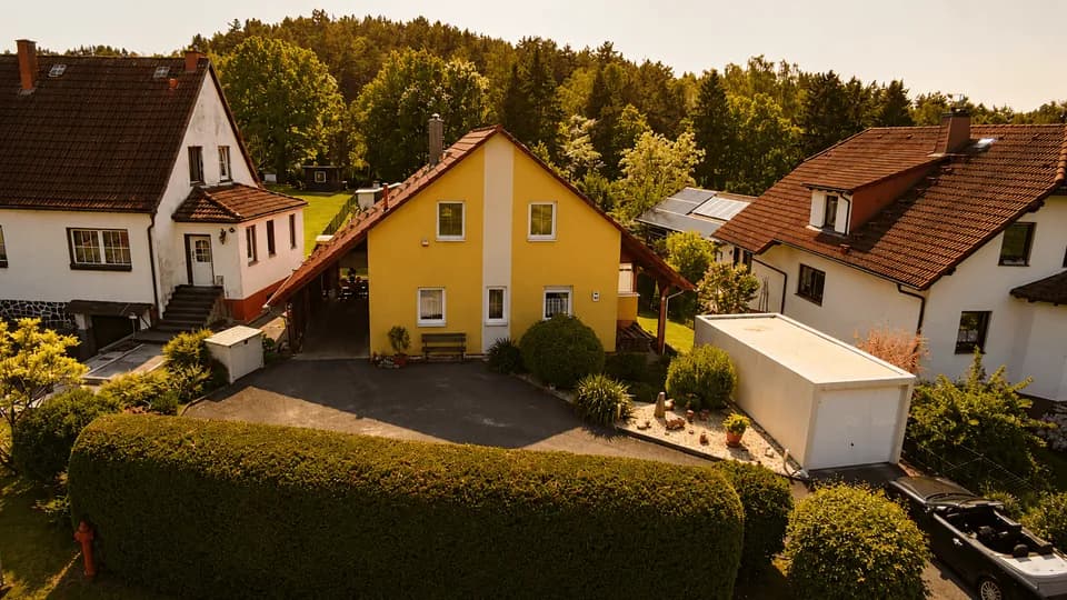 Luftaufnahme des Einfamilienhauses mit großem Gartengrundstück, eingezäunter Rasenfläche und Blick ins Grüne.