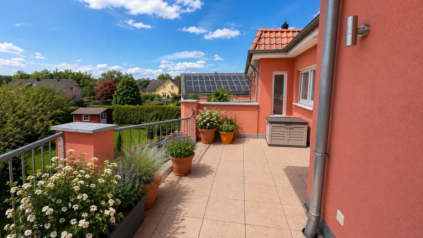 Großzügige geflieste Dachterrasse mit Geländer, Gartentruhe, üppiger Blütenbepflanzung und herrlichem Weitblick in den Garten und die Nachbarschaft.