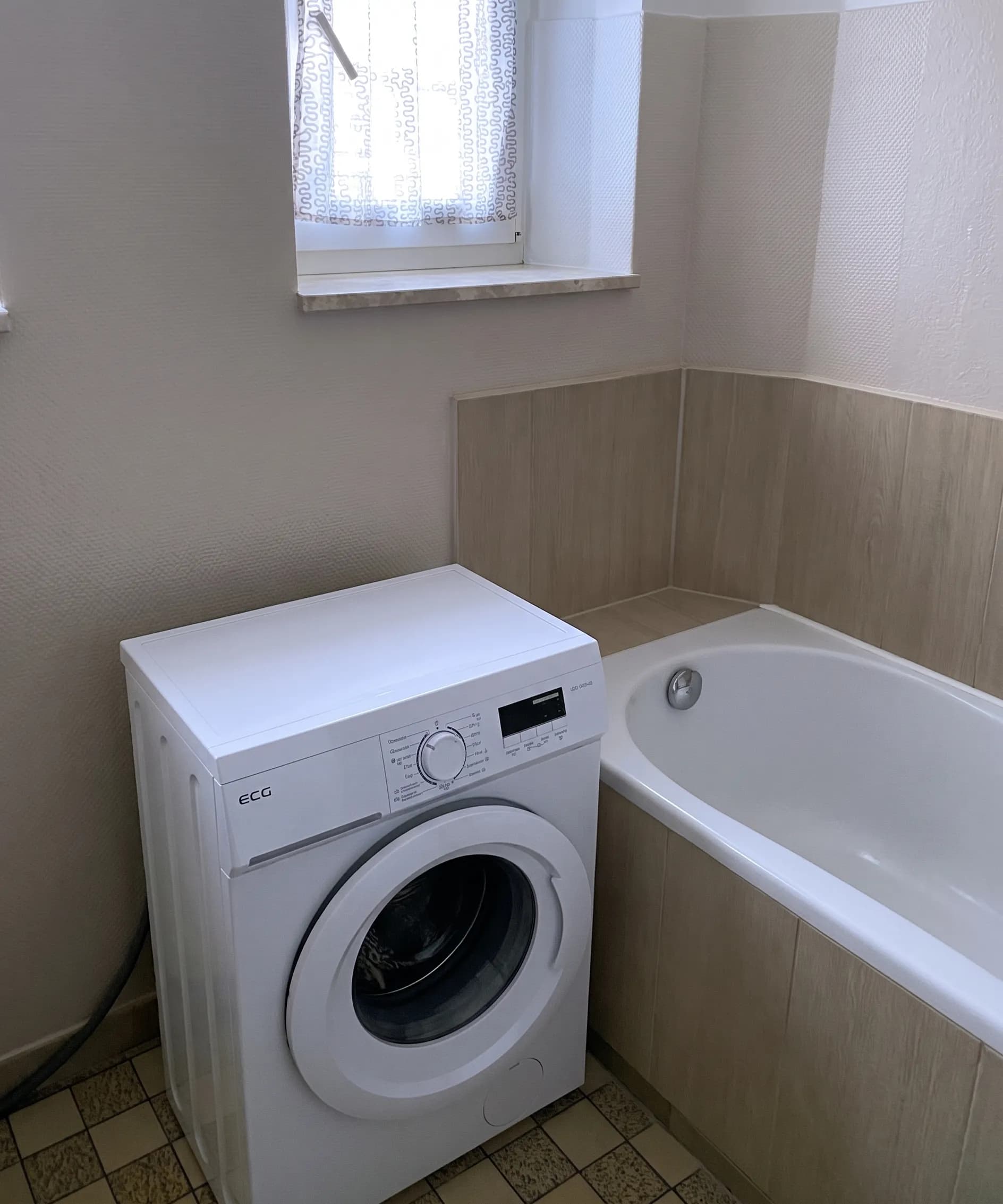 Kompaktes Tageslichtbad mit Badewanne, Waschmaschine, Warmwasserboiler und gefliestem Boden.