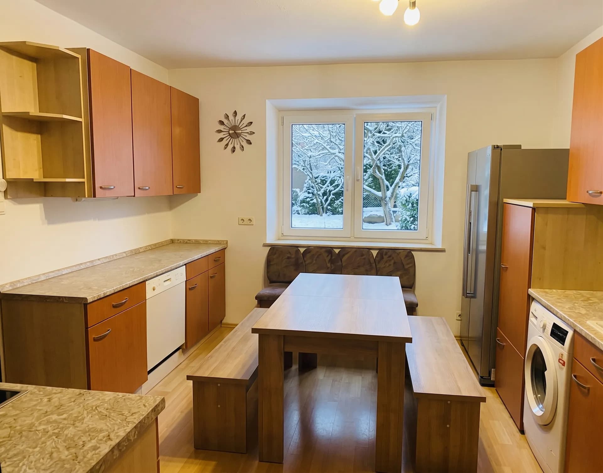 Geräumige Wohnküche mit Holzfronten, massiver Essgruppe mit Sitzbänken, modernen Elektrogeräten und großem Fenster mit Blick in den Garten.