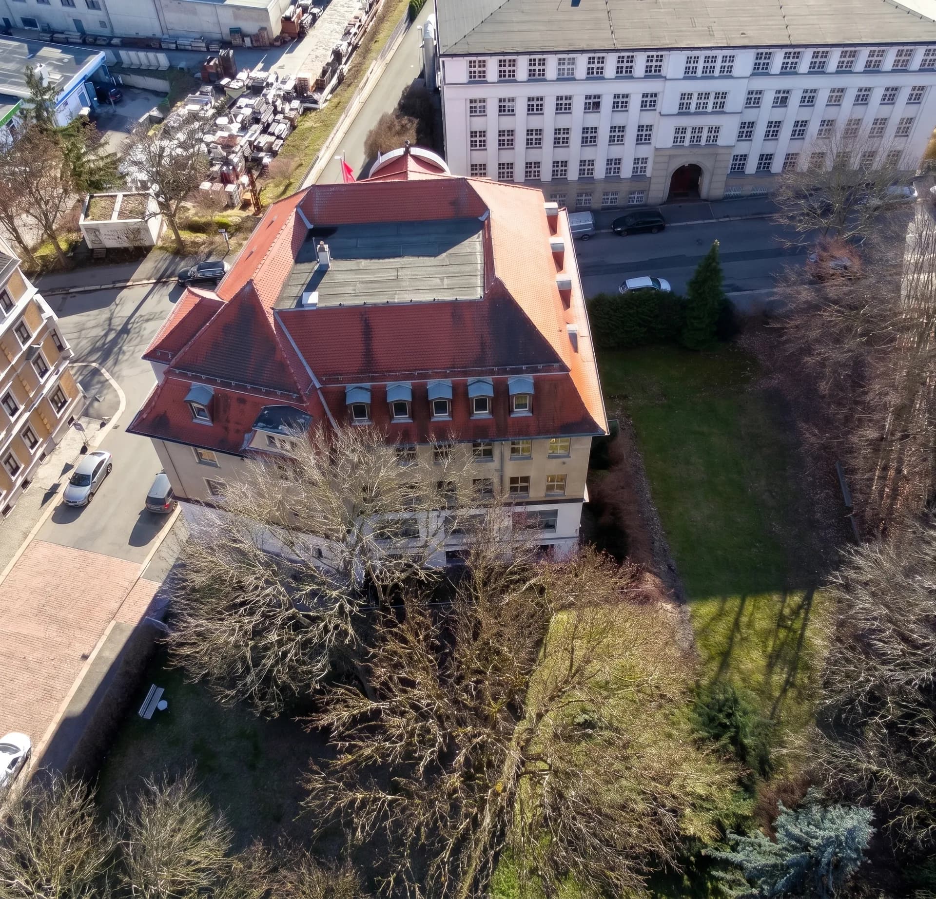 Vogelperspektive des Gebäudekomplexes mit Mansarddach, Gaubenreihen, begrüntem Innenhof samt altem Baumbestand und angrenzenden Verwaltungsbauten.