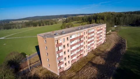 Mehrstöckiges Plattenbau-Wohnhaus in idyllischer Wald- und Wiesenlage: Vogelperspektive auf Fassade mit Balkonen, Flachdach und umliegendes Grundstück