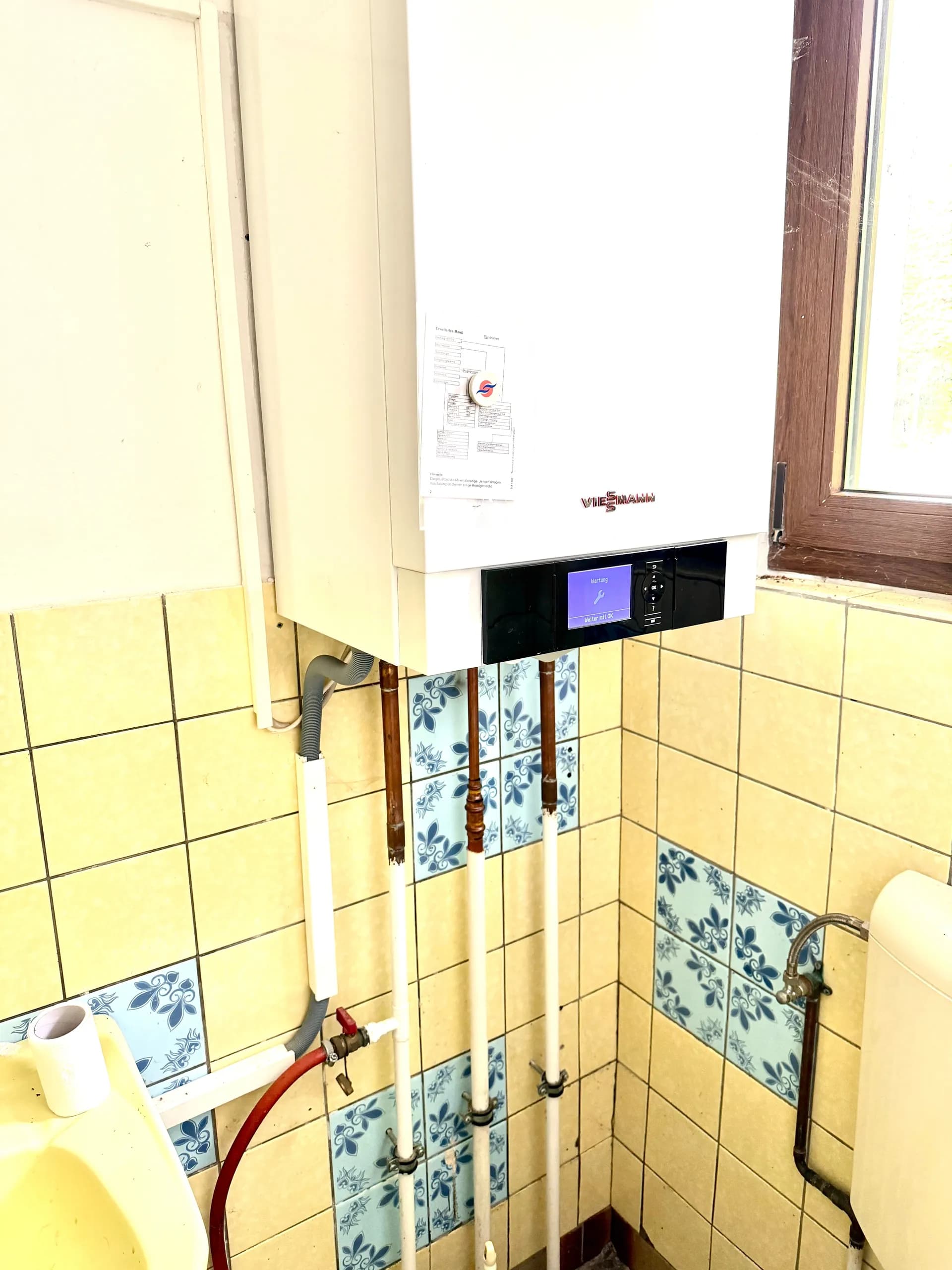 Moderne wandhängende Viessmann-Gastherme mit digitalem Bedienfeld und sichtbarer Verrohrung im Sanitär-/Technikbereich.