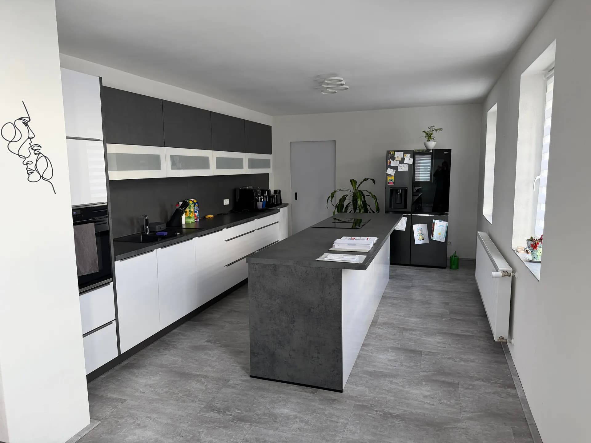 Großzügige moderne Designerküche mit freistehendem Küchenblock, kontrastreichen Fronten, hochwertigen Einbaugeräten und Side-by-Side-Kühlschrank.