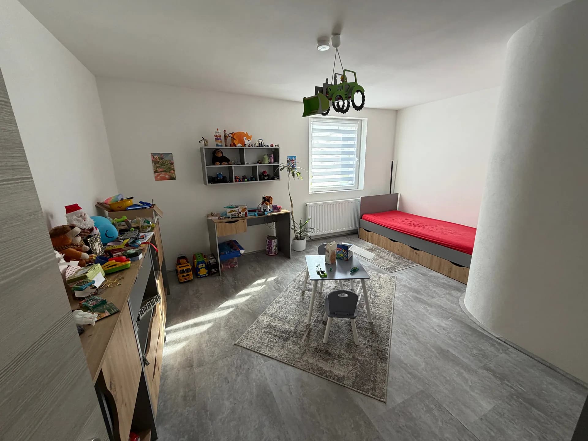 Großes, lichtdurchflutetes Kinderzimmer mit Einzelbett, Schreibtisch, Stauraummöbeln und charakteristischer runder Wandsäule.