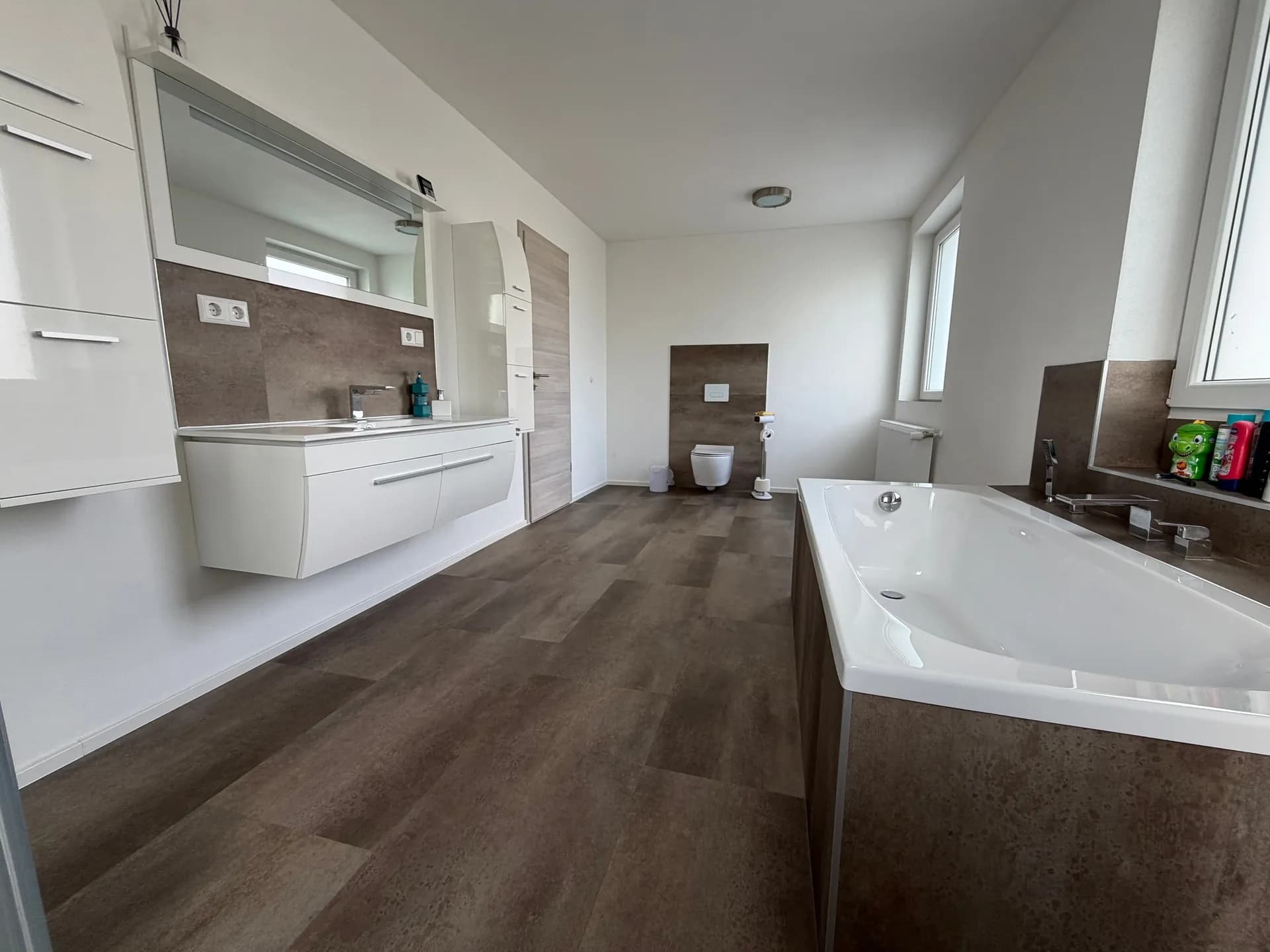 Exklusives, modernes Tageslichtbad mit großer Badewanne, elegantem Waschtisch mit beleuchtetem Spiegelschrank, Hänge-WC und stilvoller Schiefer-/Steinoptik.
