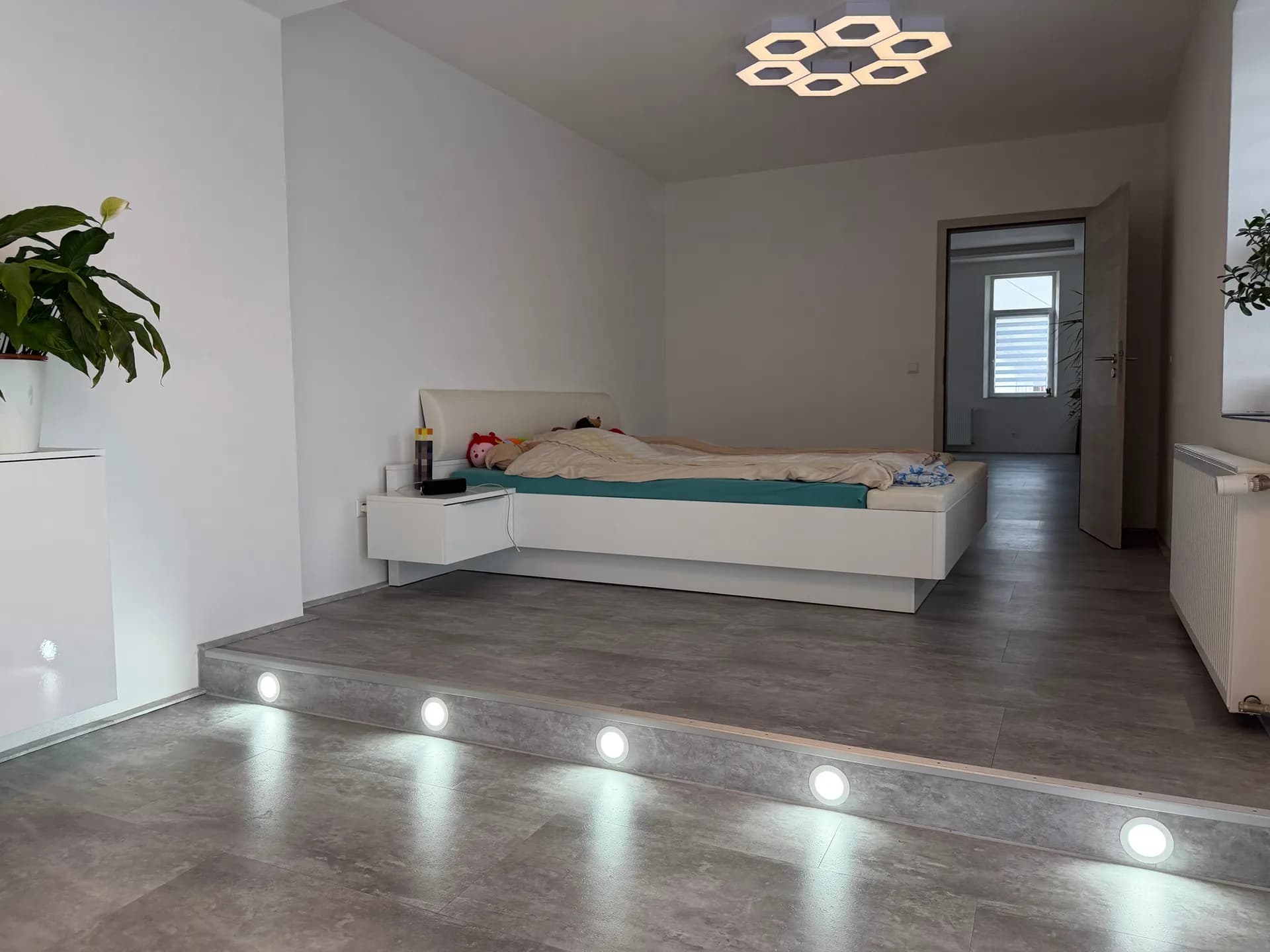 Eindrucksvolles Hauptschlafzimmer auf Podestebene mit integrierten LED-Bodenstrahlern, moderner Deckenleuchte und großzügigem Raumgefühl.