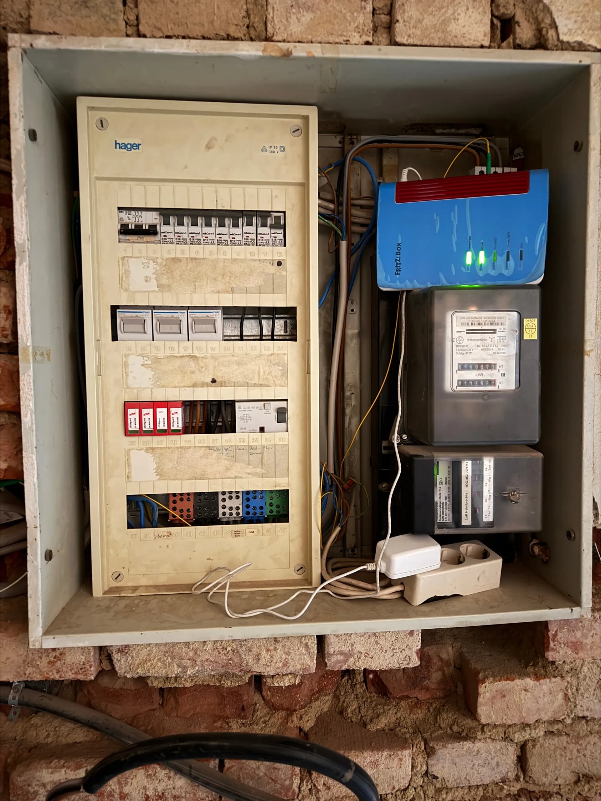 Elektro-Sicherungskasten von Hager mit Leitungsschutzschaltern, digitalem Stromzähler und angeschlossenem FRITZ!Box-Router im Technikbereich.