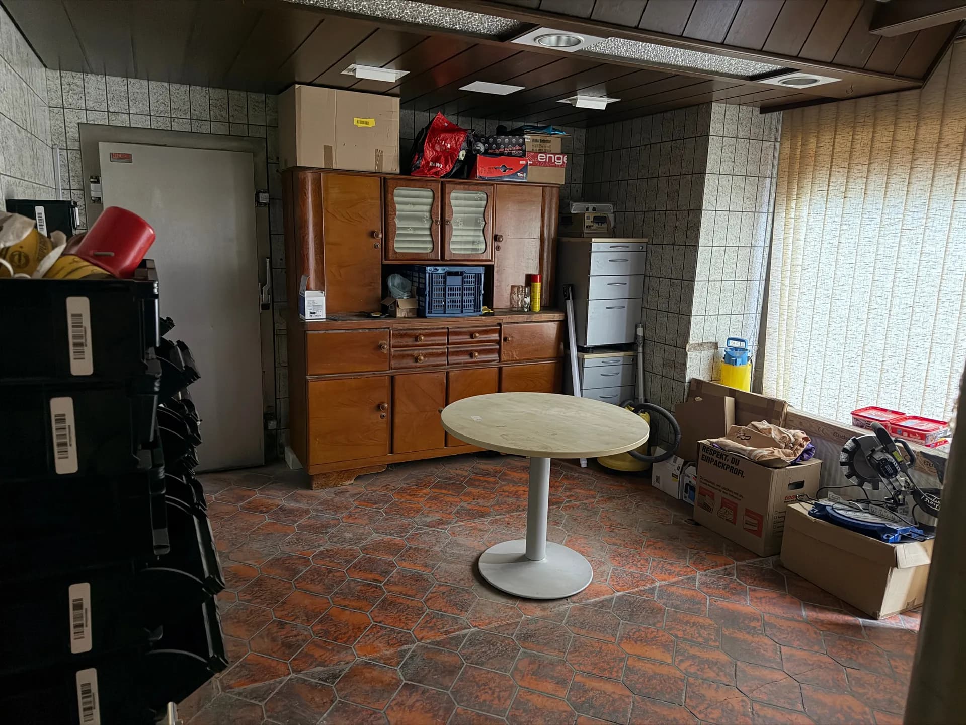Großzügiger Werkstatt- oder Hauswirtschaftsraum mit rustikalem Fliesenboden, Holzdeckenverkleidung, historischem Küchenbuffet und rundem Tisch.