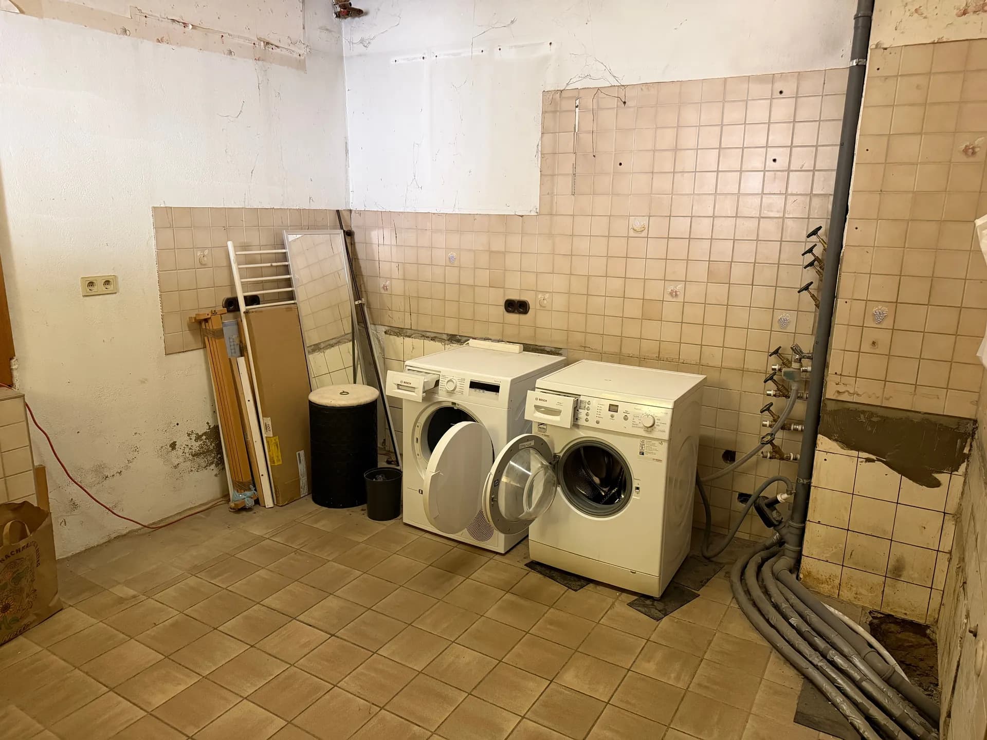 Funktionale Waschküche / Hauswirtschaftsraum im Untergeschoss mit Fliesenboden, Waschmaschinenanschlüssen, Waschmaschine und Trockner.
