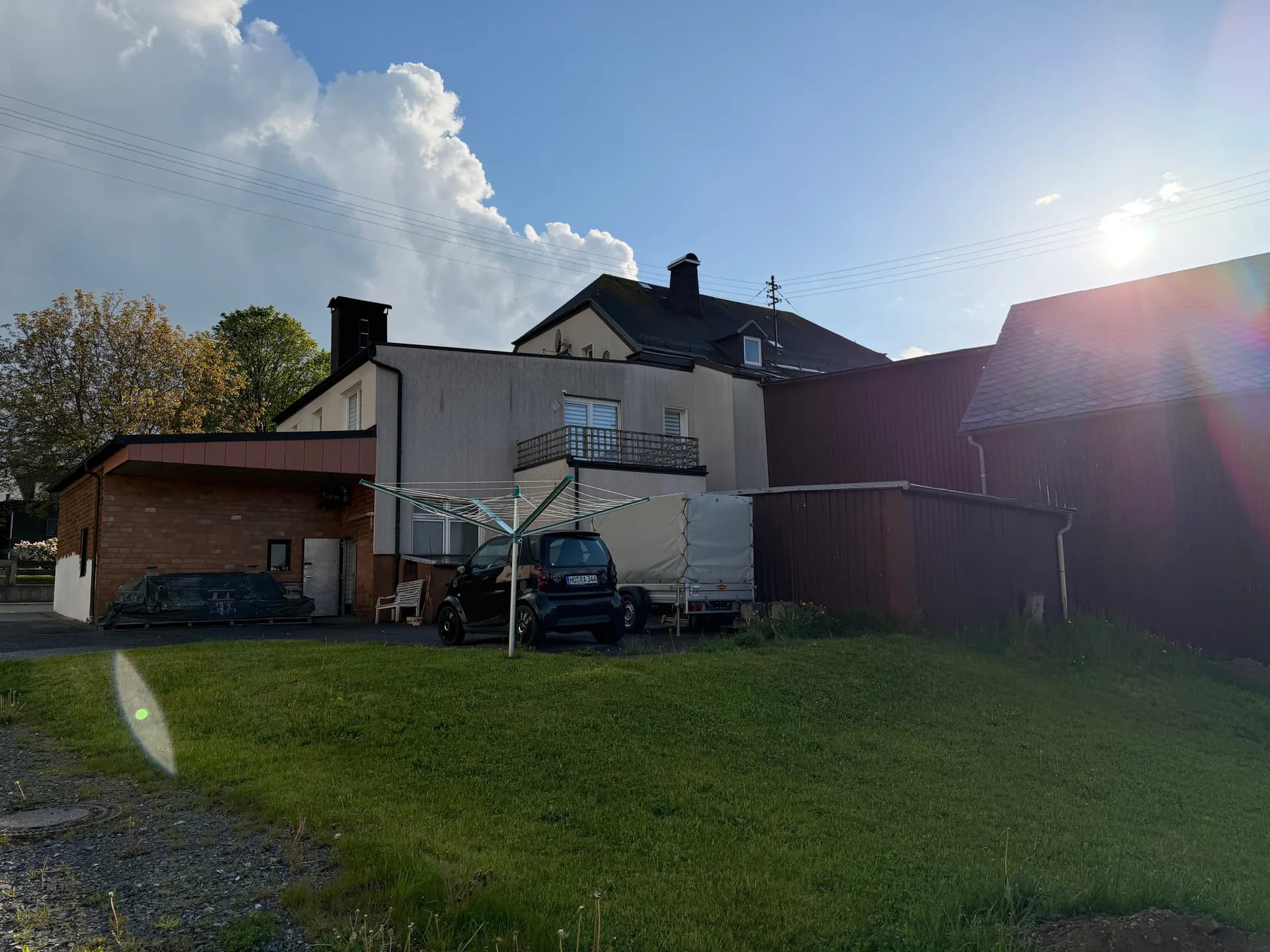 Rückansicht des Anwesens mit Gartenwiese, Stellplatzbereich, Nebengebäuden und sonniger Dachterrasse im Obergeschoss.