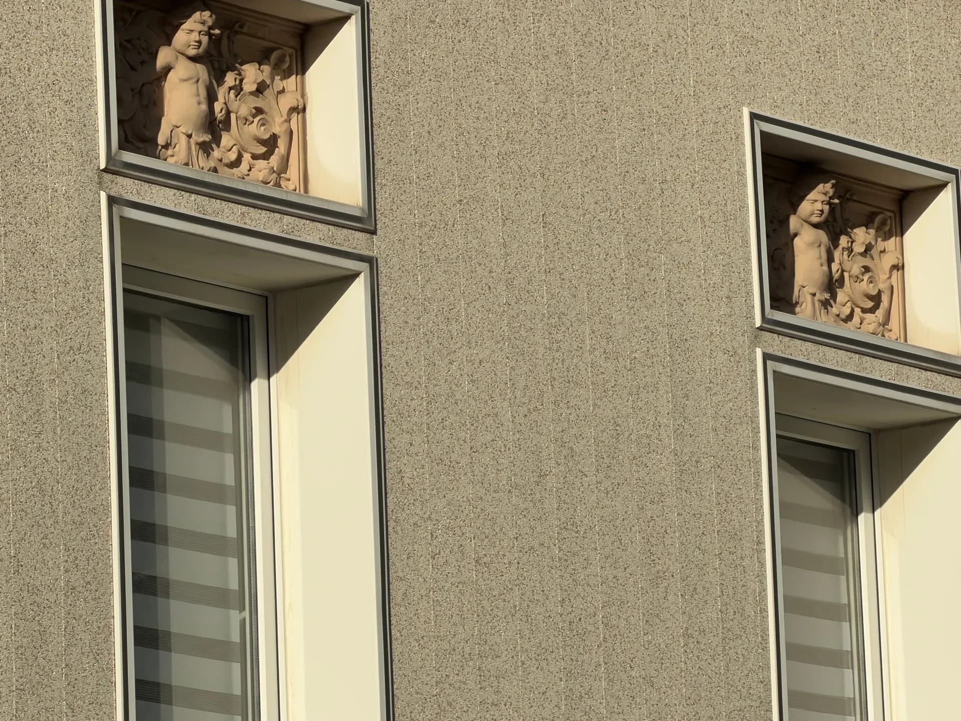 Historische Fassadendetails: kunstvolle Relief-Ornamente über den Fensterelementen mit modernen Isolierglasfenstern.