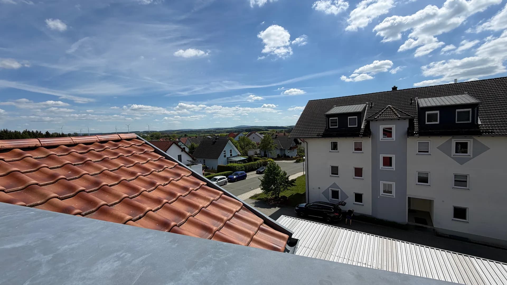 Weitläufiger Ausblick von der Dachterrasse über Ziegeldächer, eine gepflegte Wohnsiedlung und die grüne Landschaft.
