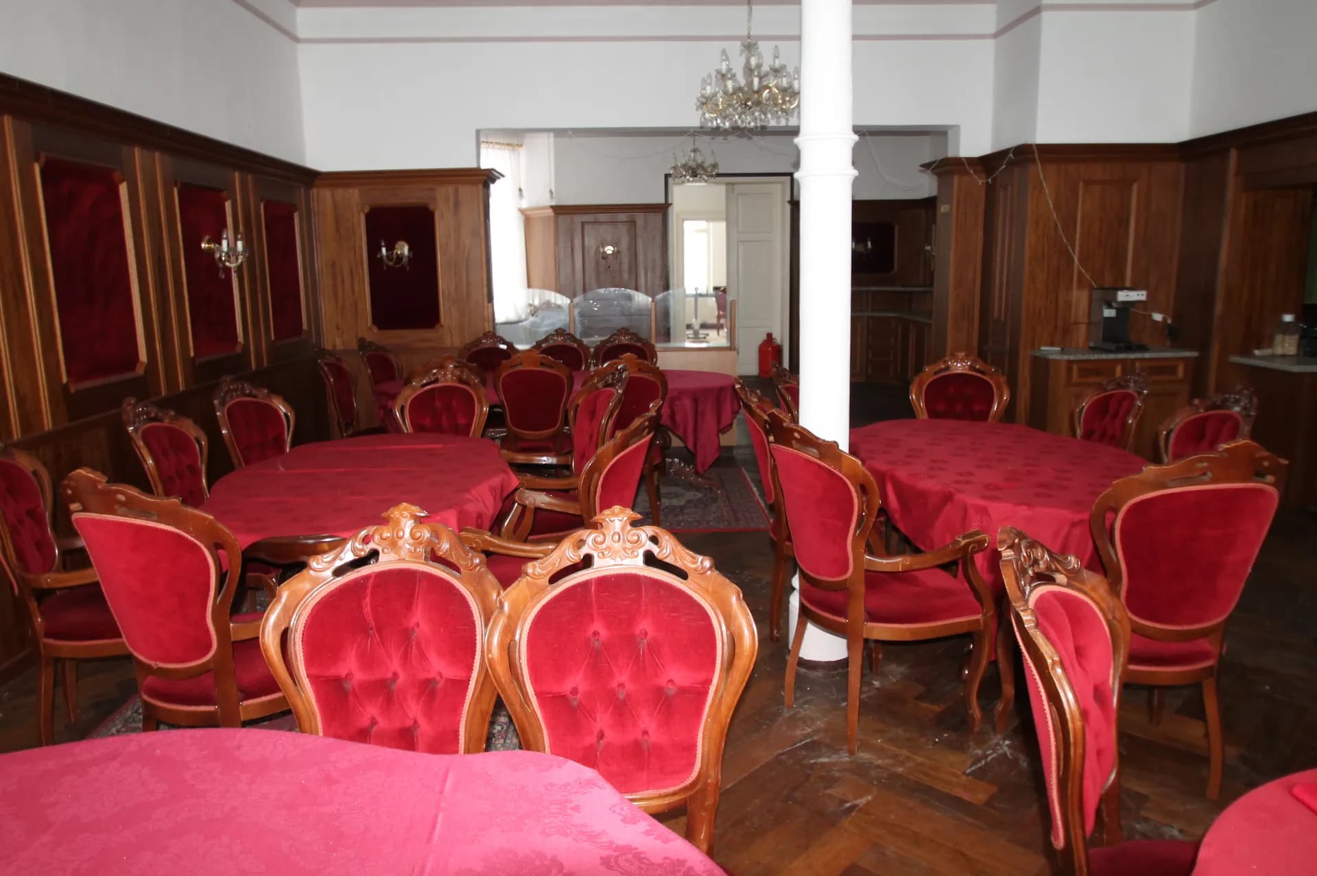 Traditioneller Gast- oder Restaurantbereich im rustikalen Holzstil mit Wandvertäfelung, eingedeckten Rundtischen mit roten Tischdecken, Barockstil-Polsterstühlen und weißer Mittelsäule.