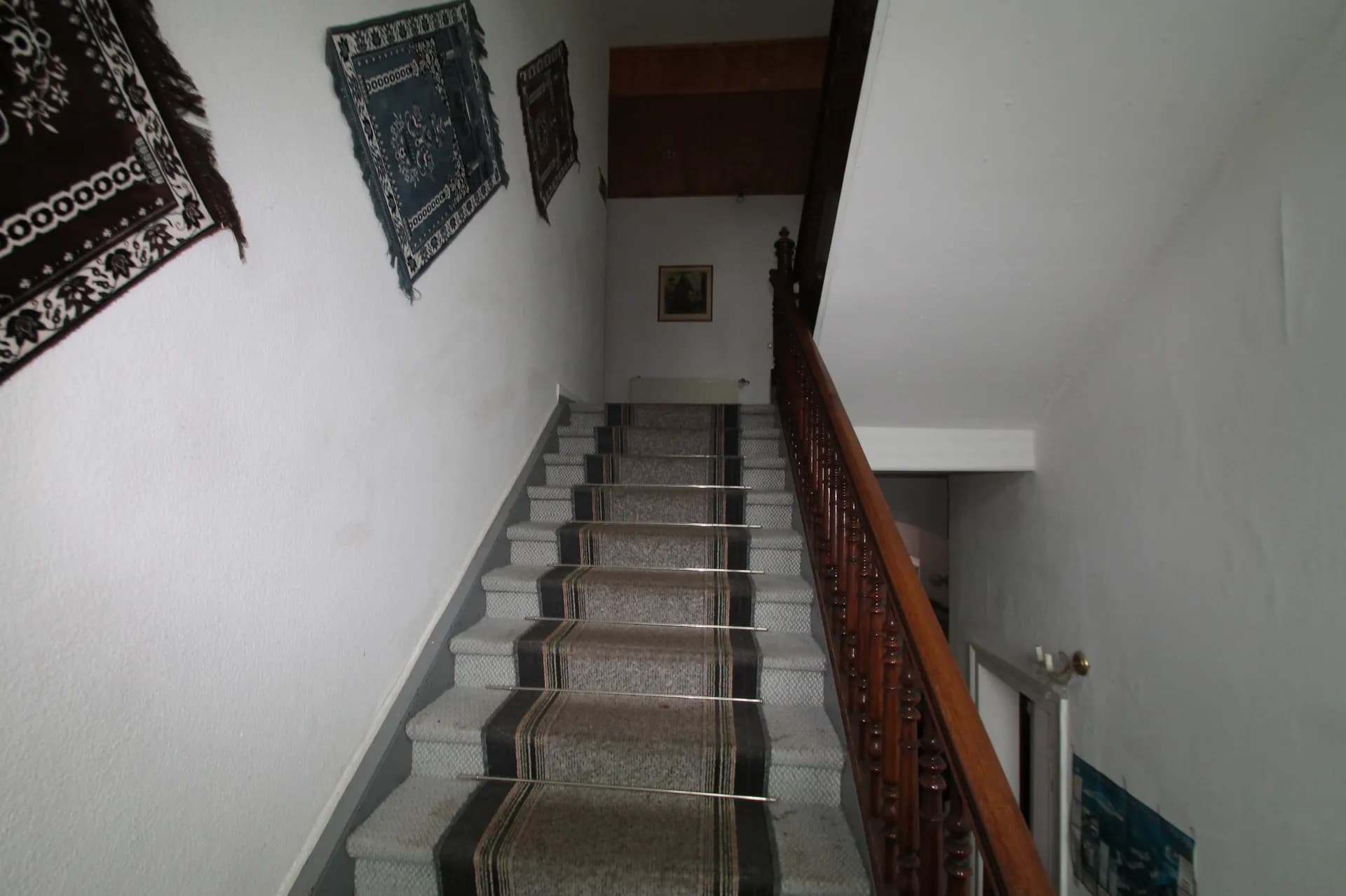 Internes Treppenhaus des Hotelbereichs mit teppichbelegten Steinstufen, Treppenstangen, gedrechseltem Holzgeländer und dekorativen Wandteppichen.