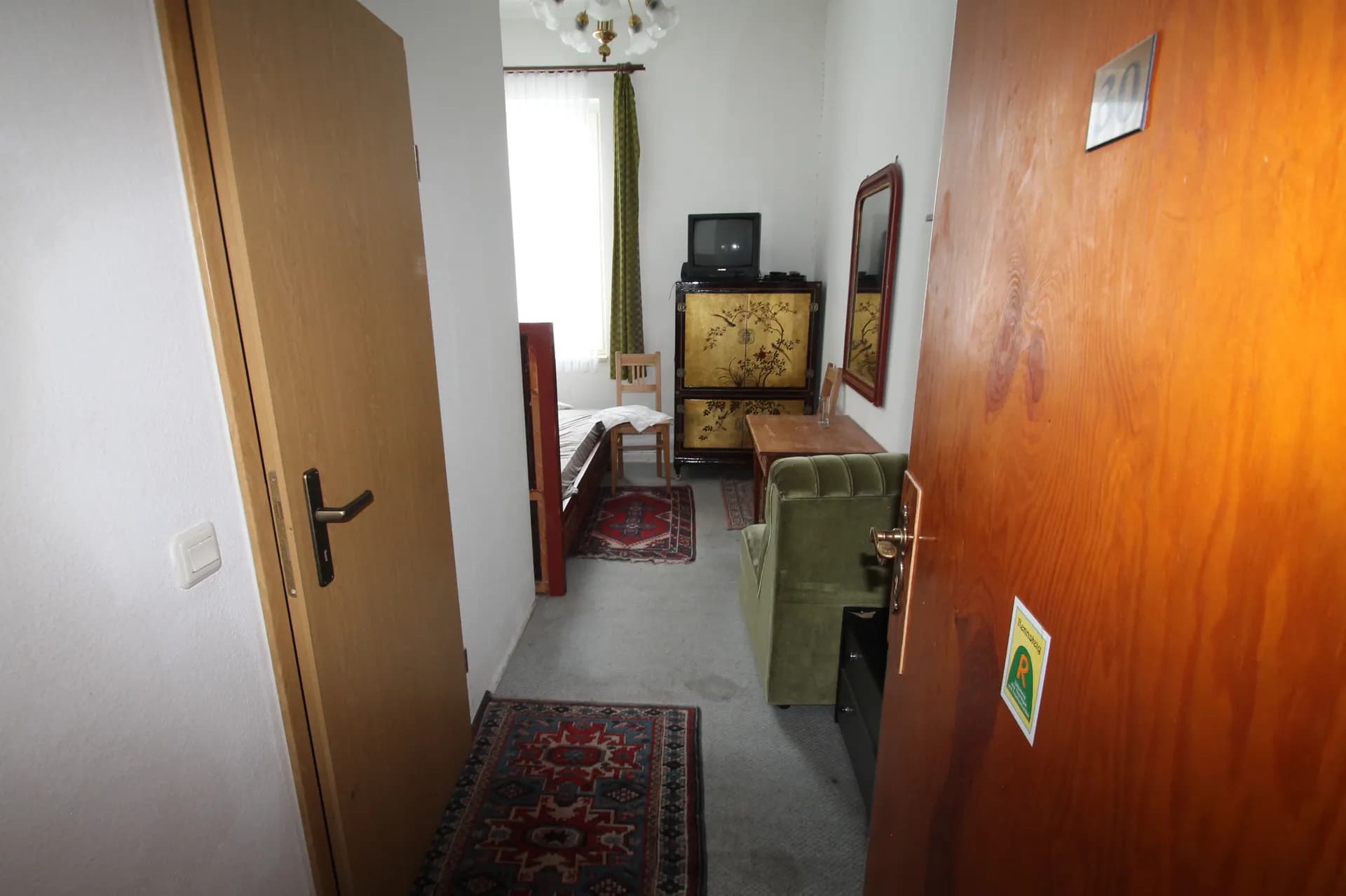 Blick durch die geöffnete Zimmertür (Zimmer 10) in das Gästezimmer mit Orientläufer, grünem Samtsessel, TV-Ecke und Zugang zum Schlafbereich.